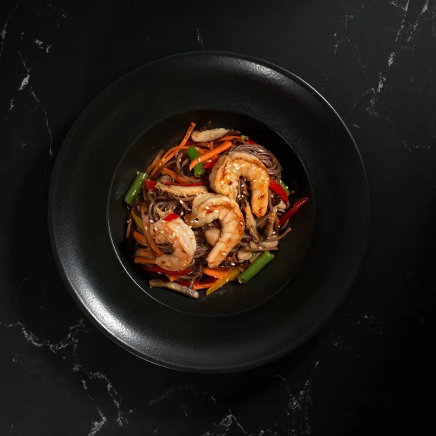 Shrimp and glass noodles with vegetables on a black plate